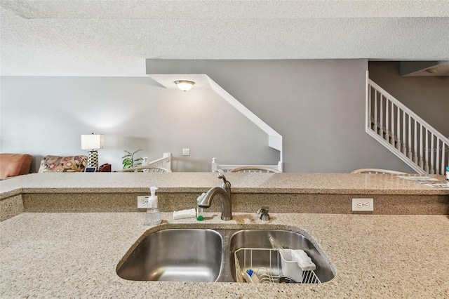 kitchen with a textured ceiling, light stone counters, and a sink