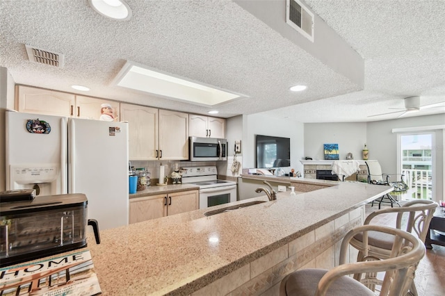 kitchen with white appliances, visible vents, a kitchen breakfast bar, and a sink