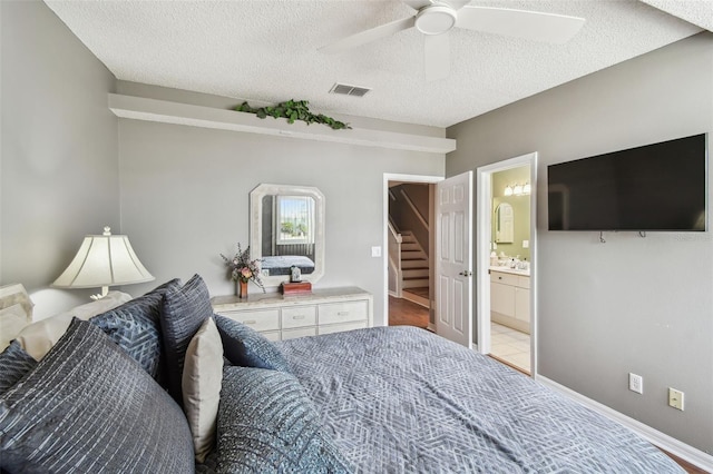 bedroom featuring baseboards, visible vents, ceiling fan, ensuite bathroom, and a textured ceiling