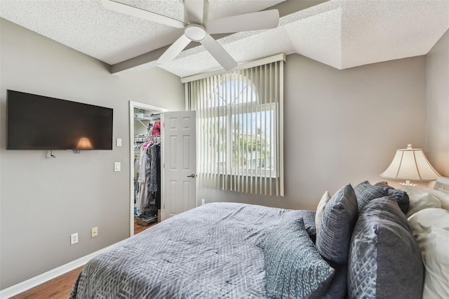 bedroom featuring lofted ceiling, a spacious closet, a textured ceiling, wood finished floors, and baseboards