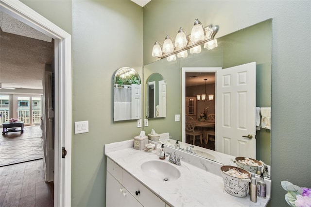 bathroom with a textured ceiling, wood finished floors, vanity, and a notable chandelier