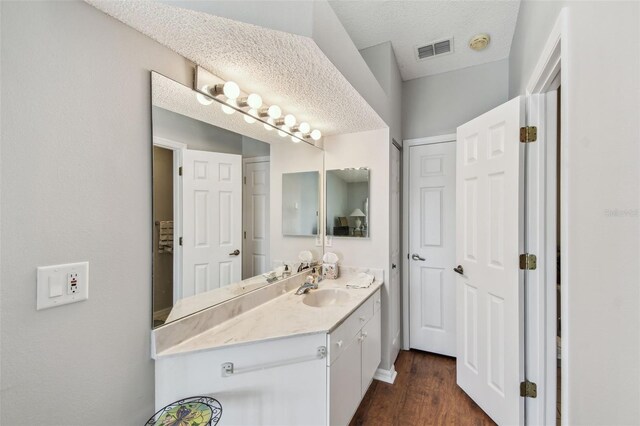 bathroom with a textured ceiling, visible vents, wood finished floors, and vanity