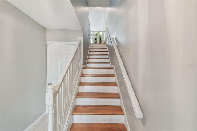 stairs featuring a textured ceiling, tile patterned flooring, and baseboards