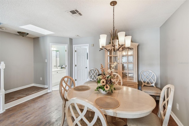 dining space with a skylight, a textured ceiling, baseboards, and wood finished floors