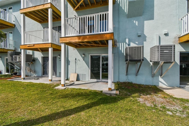 rear view of property with a yard, central air condition unit, a patio area, and stucco siding