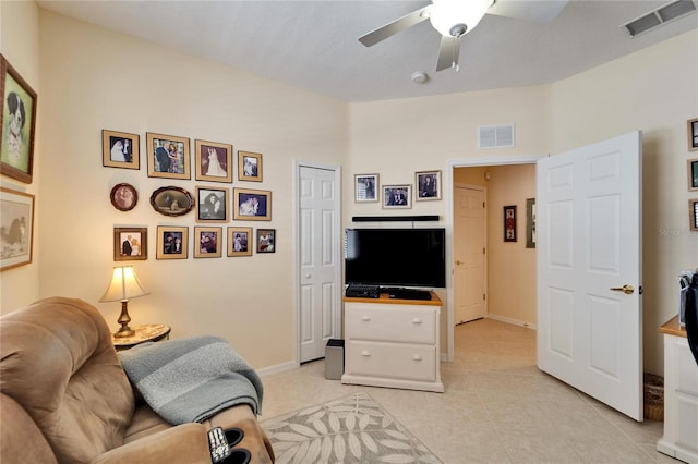 living area with light tile patterned floors, ceiling fan, visible vents, and baseboards