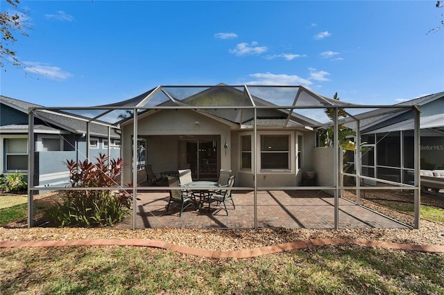 rear view of property featuring glass enclosure, stucco siding, and a patio