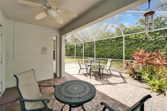 view of patio / terrace featuring glass enclosure, outdoor dining space, and a ceiling fan