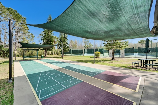 view of community with a tennis court, fence, shuffleboard, and a yard