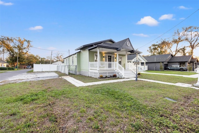 view of front facade featuring covered porch, roof with shingles, fence, and a front yard