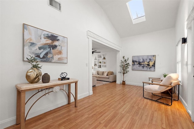 sitting room featuring vaulted ceiling with skylight, light wood-type flooring, visible vents, and baseboards