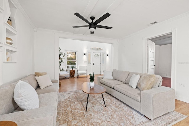 living area featuring wood finished floors, visible vents, baseboards, a ceiling fan, and ornamental molding