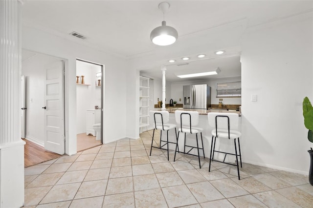 kitchen with decorative columns, stainless steel fridge with ice dispenser, visible vents, a peninsula, and a kitchen bar