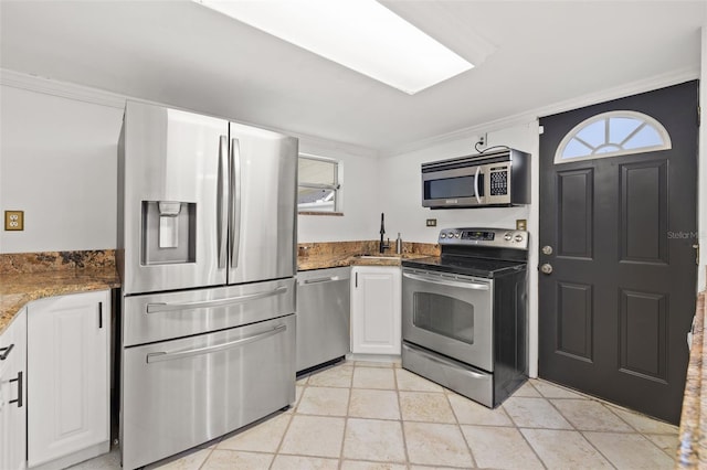 kitchen featuring stainless steel appliances, a sink, white cabinetry, dark stone counters, and crown molding