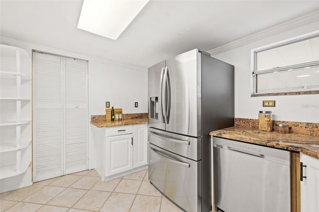 kitchen featuring light tile patterned floors, stone counters, stainless steel appliances, white cabinetry, and ornamental molding