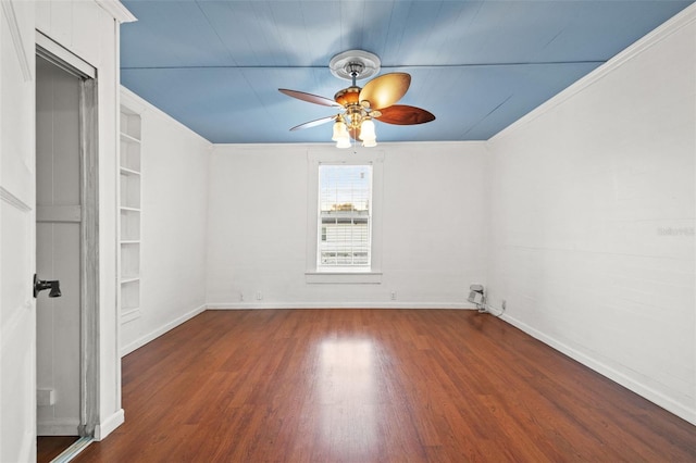 spare room with ceiling fan, built in shelves, wood finished floors, baseboards, and ornamental molding