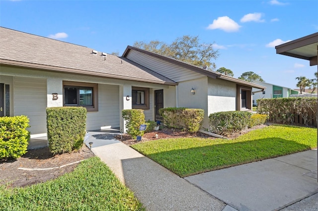 ranch-style home with a shingled roof, a front lawn, and stucco siding