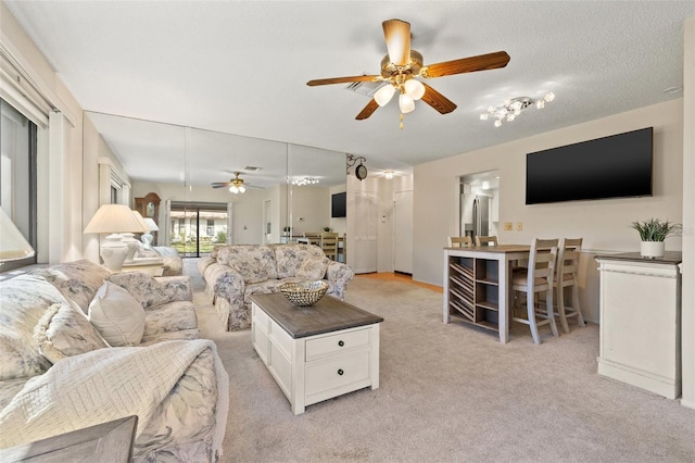 living area featuring a ceiling fan, light carpet, and a textured ceiling