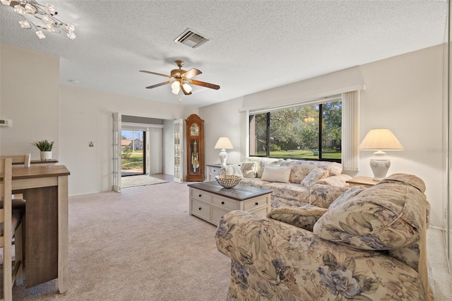 living room featuring a textured ceiling, visible vents, a ceiling fan, and light colored carpet