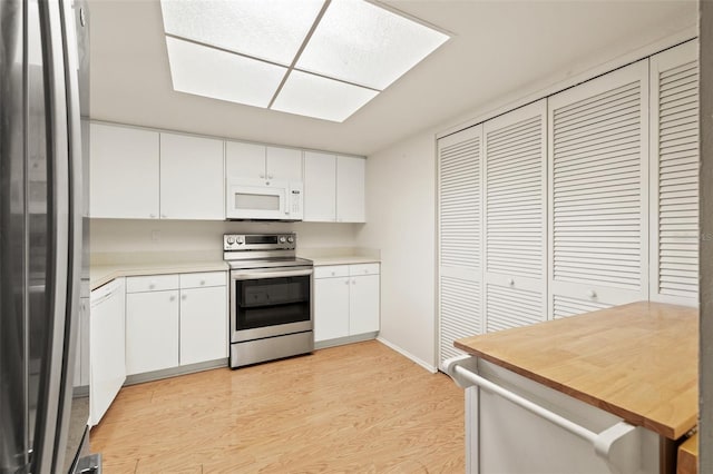 kitchen featuring a skylight, white cabinets, appliances with stainless steel finishes, light countertops, and light wood-type flooring