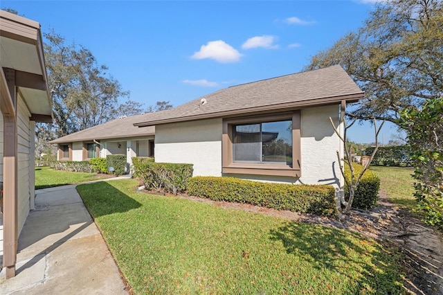 view of front of home with a shingled roof, a front yard, and stucco siding