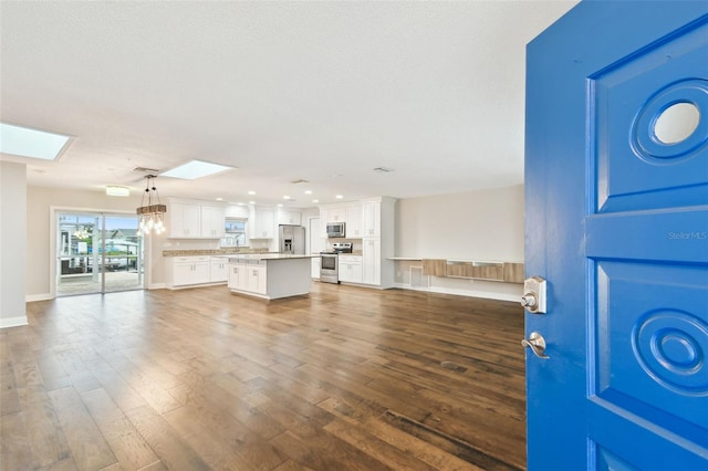 unfurnished living room featuring recessed lighting, a skylight, dark wood-type flooring, and baseboards