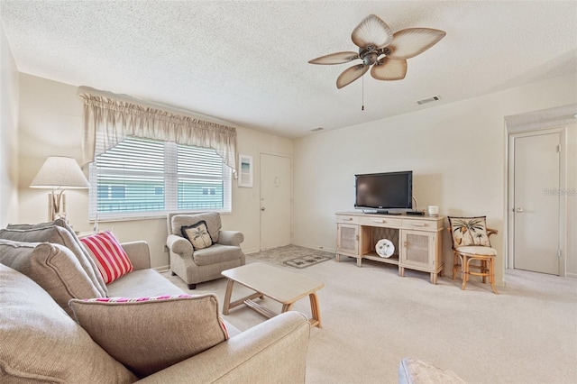 living room with a textured ceiling, carpet floors, visible vents, and a ceiling fan