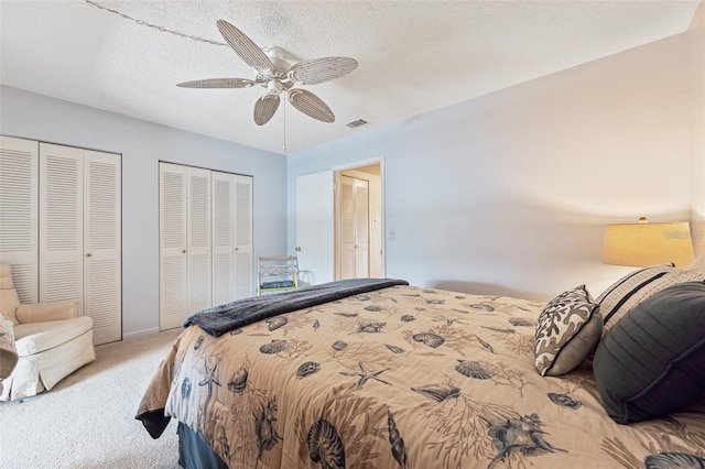 bedroom featuring a textured ceiling, visible vents, a ceiling fan, carpet, and two closets