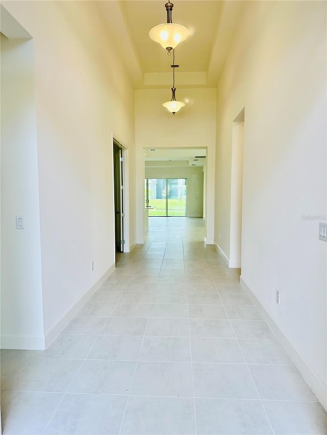 hall featuring light tile patterned flooring, a raised ceiling, a towering ceiling, and baseboards