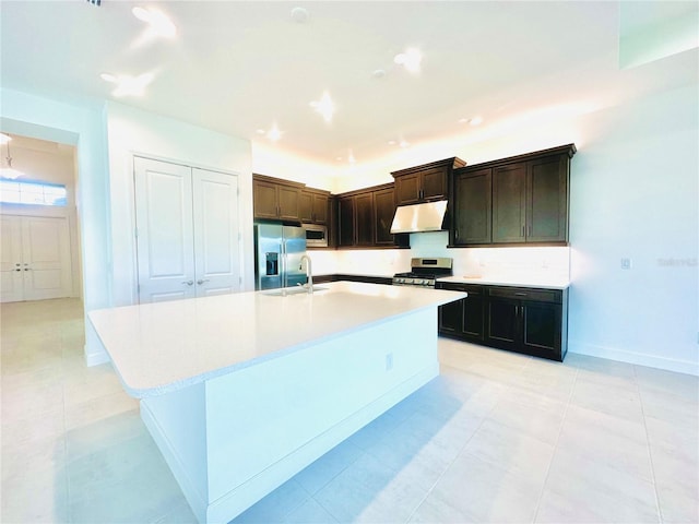 kitchen featuring dark brown cabinetry, a center island with sink, appliances with stainless steel finishes, light countertops, and under cabinet range hood