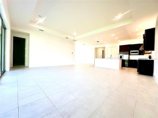 unfurnished living room featuring a sink, light tile patterned flooring, and a raised ceiling