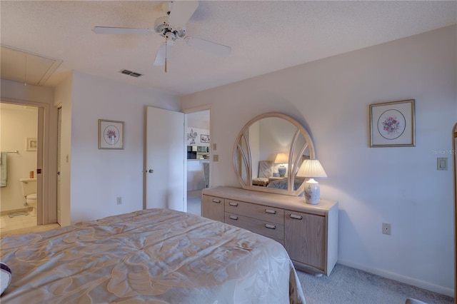 bedroom with light colored carpet, visible vents, ensuite bathroom, attic access, and a ceiling fan