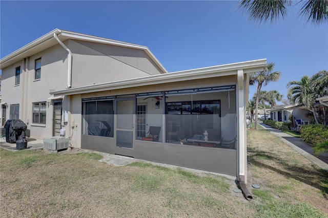 rear view of property with a lawn, a sunroom, and stucco siding