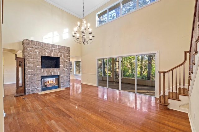 unfurnished living room featuring crown molding, a brick fireplace, a notable chandelier, and wood finished floors