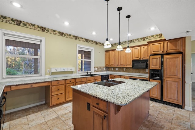 kitchen featuring brown cabinetry, a center island, light stone countertops, black appliances, and a sink