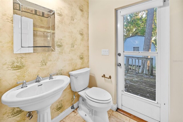 bathroom with toilet, wallpapered walls, baseboards, and a sink