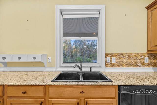 kitchen with dishwasher, backsplash, a sink, and light stone countertops