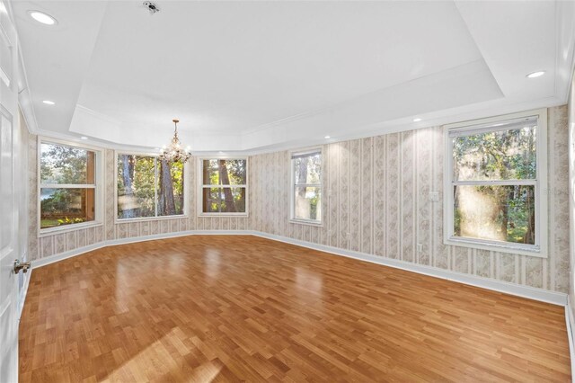 interior space with a tray ceiling, light wood finished floors, a chandelier, baseboards, and wallpapered walls