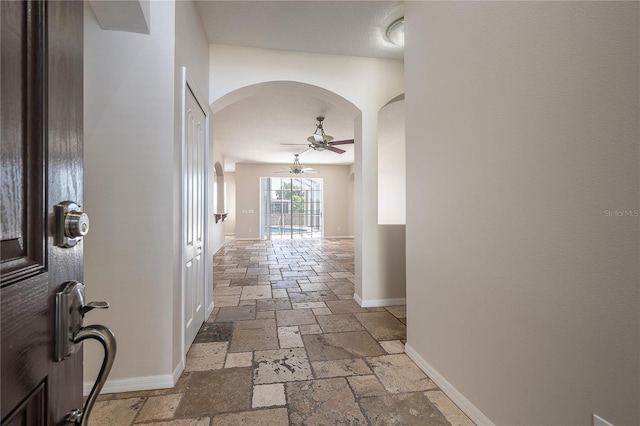 hallway with arched walkways, stone tile flooring, and baseboards