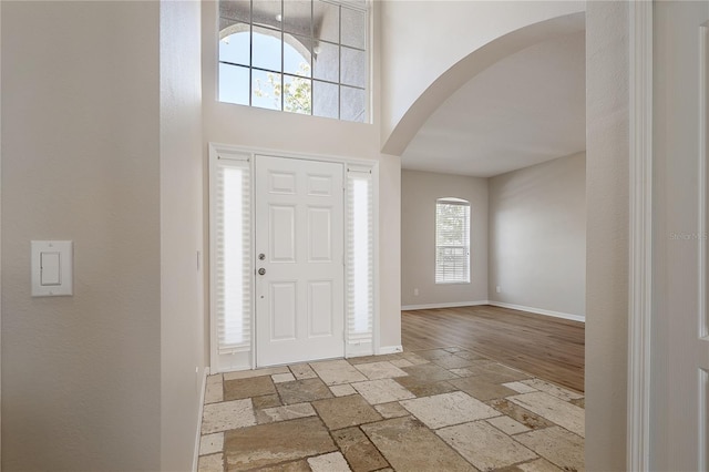 foyer entrance with arched walkways, stone tile floors, a towering ceiling, and baseboards