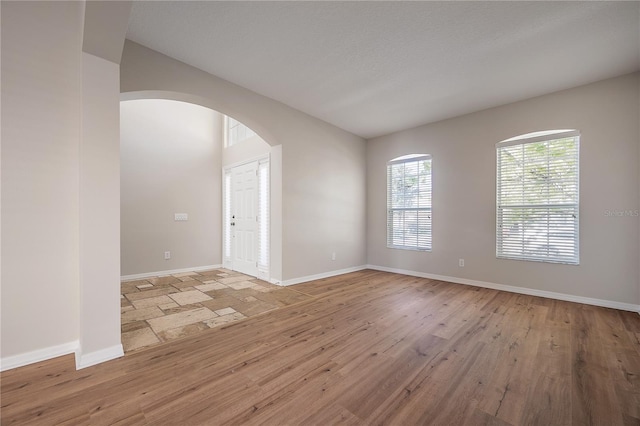 unfurnished room with baseboards, arched walkways, and wood finished floors