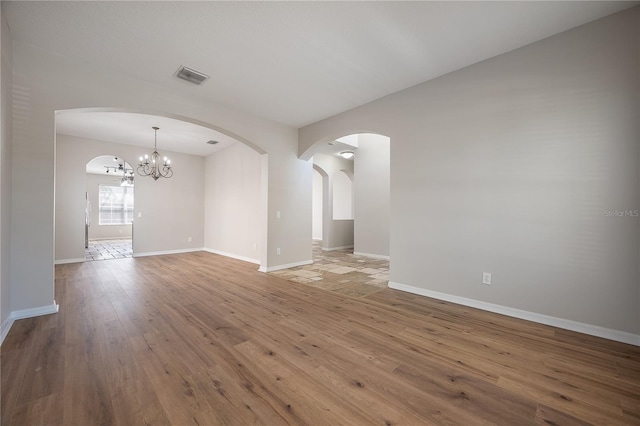 unfurnished room with arched walkways, visible vents, baseboards, hardwood / wood-style floors, and an inviting chandelier