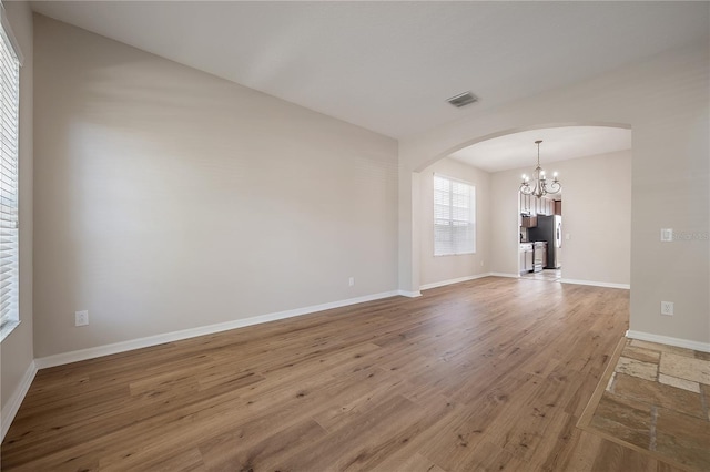 unfurnished room featuring arched walkways, a chandelier, visible vents, baseboards, and light wood-style floors