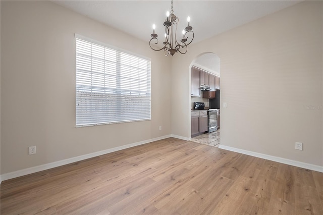 empty room featuring arched walkways, light wood-style floors, a chandelier, and baseboards