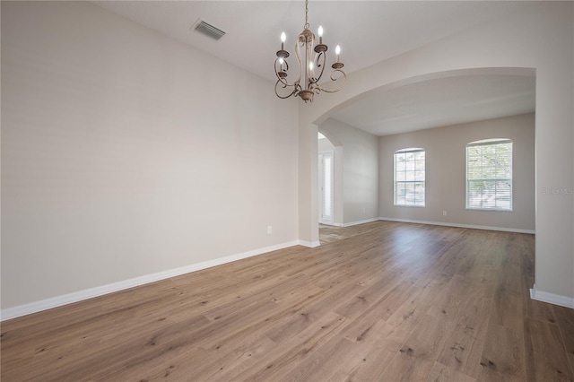 unfurnished room with arched walkways, a notable chandelier, wood finished floors, visible vents, and baseboards