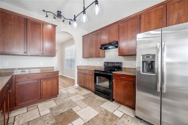 kitchen featuring arched walkways, stone tile flooring, black electric range, under cabinet range hood, and stainless steel refrigerator with ice dispenser