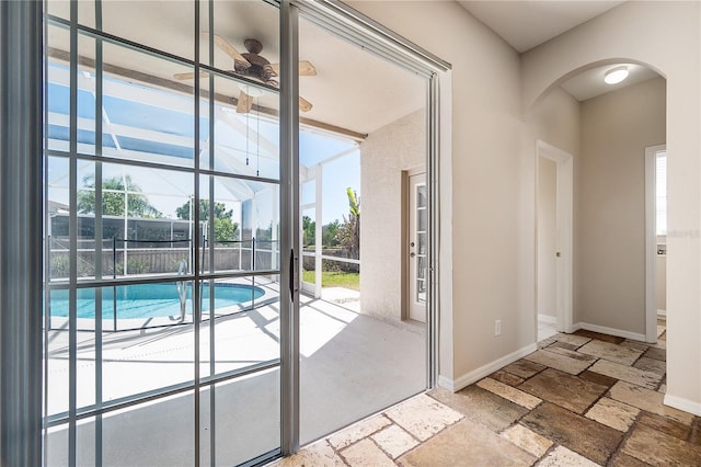 doorway with a ceiling fan, arched walkways, baseboards, and stone tile floors