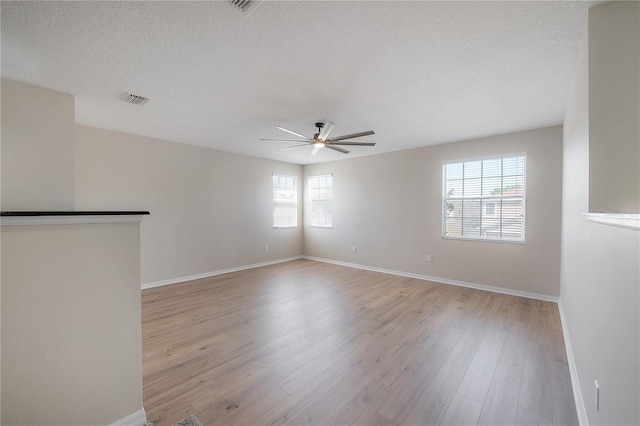 empty room with a textured ceiling, ceiling fan, visible vents, baseboards, and light wood-type flooring