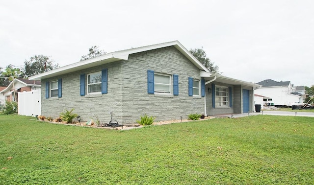 view of front of home featuring concrete driveway, fence, a garage, stone siding, and a front lawn