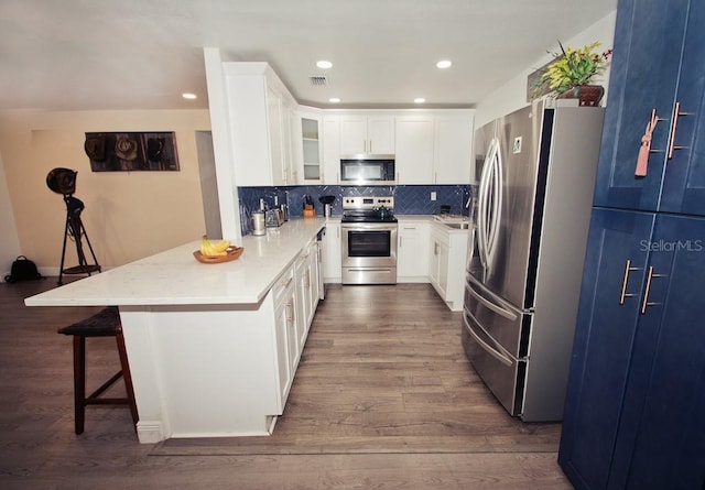 kitchen featuring a breakfast bar area, stainless steel appliances, a peninsula, backsplash, and dark wood-style floors